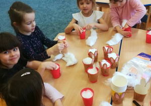 Dzieci przy stoliku wkładają do kubeczków watę, przygotowują wielkanocny upominek dla rodziców.